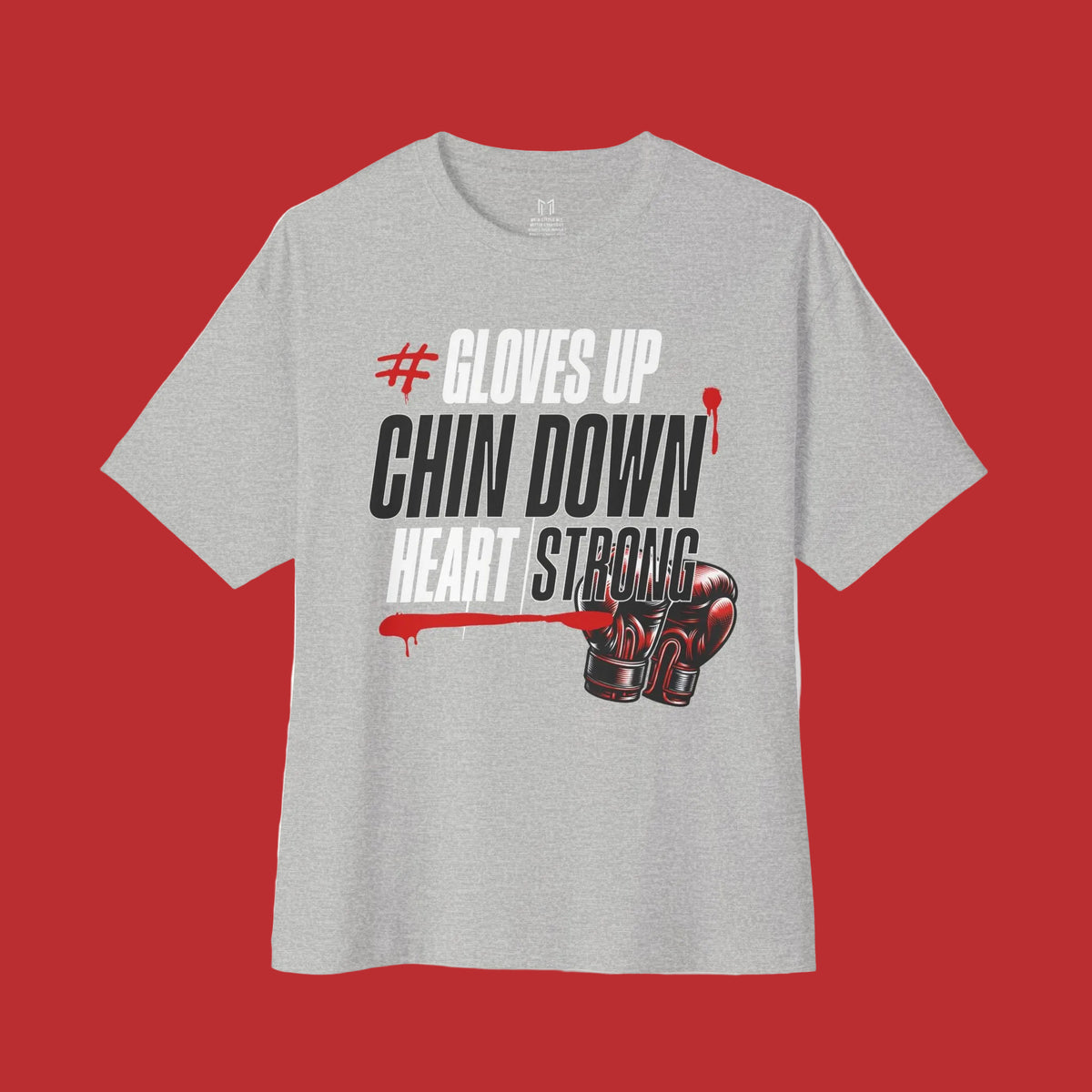 A heather gray short-sleeve t-shirt with a graphic print on the front. The graphic features the text '# GLOVES UP CHIN DOWN HEART STRONG' in black and white, with red blood-like drips and a graphic of red and black boxing gloves at the bottom right.